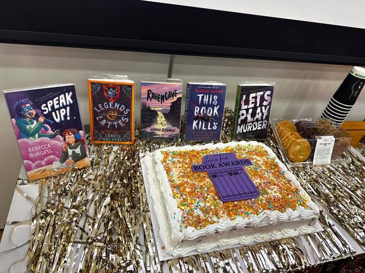 A Laurus Trust Book Awards Cake sits on a decorated table surrounded by the shortlisted books in the 2023 to 2024 competition.