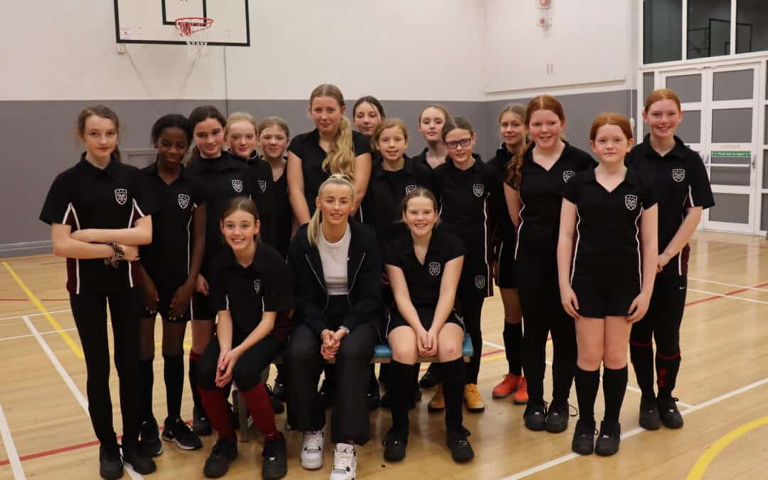Girls from Hazel Grove High School stand together in the sports hall with footballer Chloe Kelly