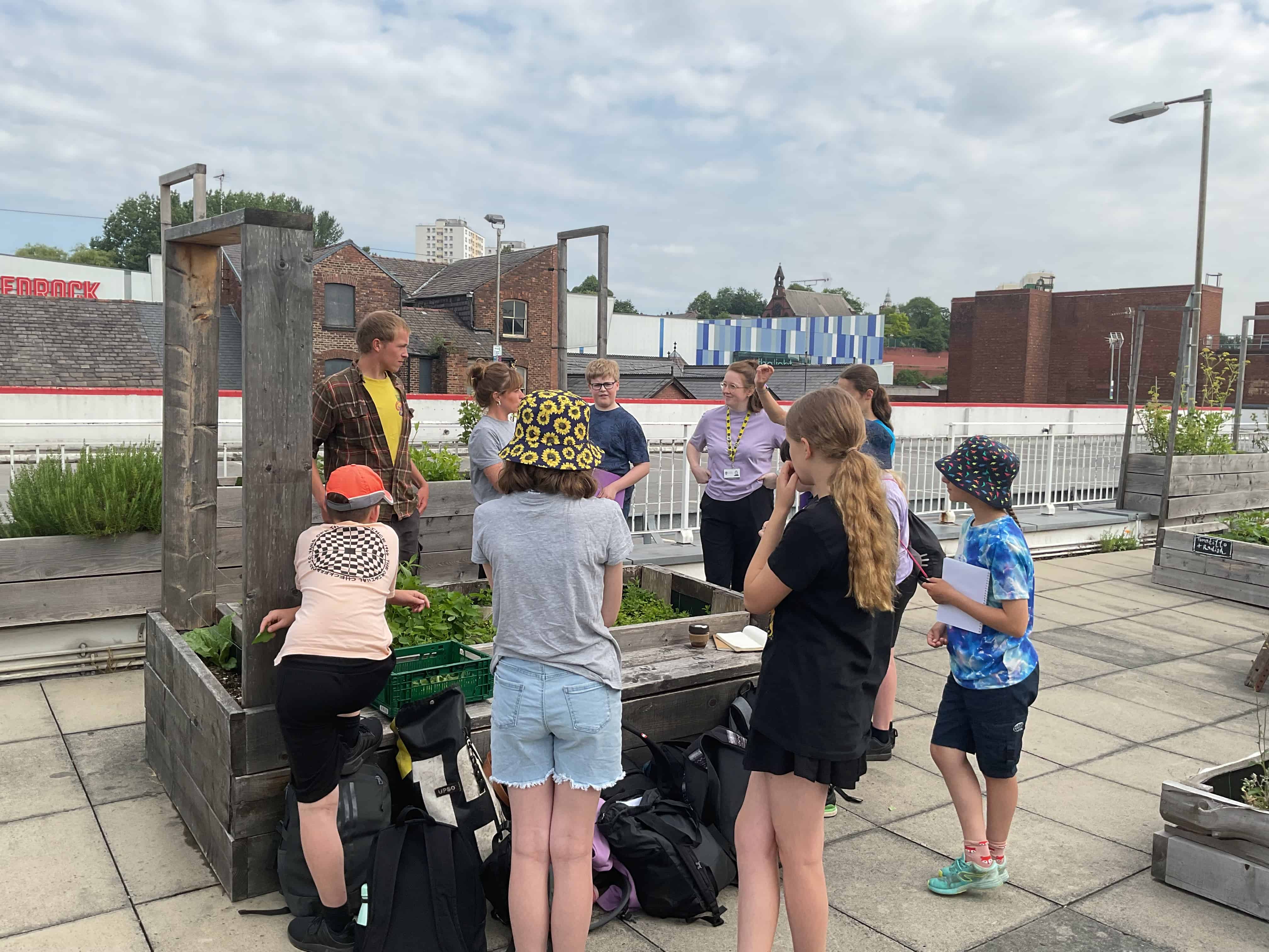 Hazel Grove High School Eco Council are gathered around a vegetable patch in The Landing, listening to a member of staff.
